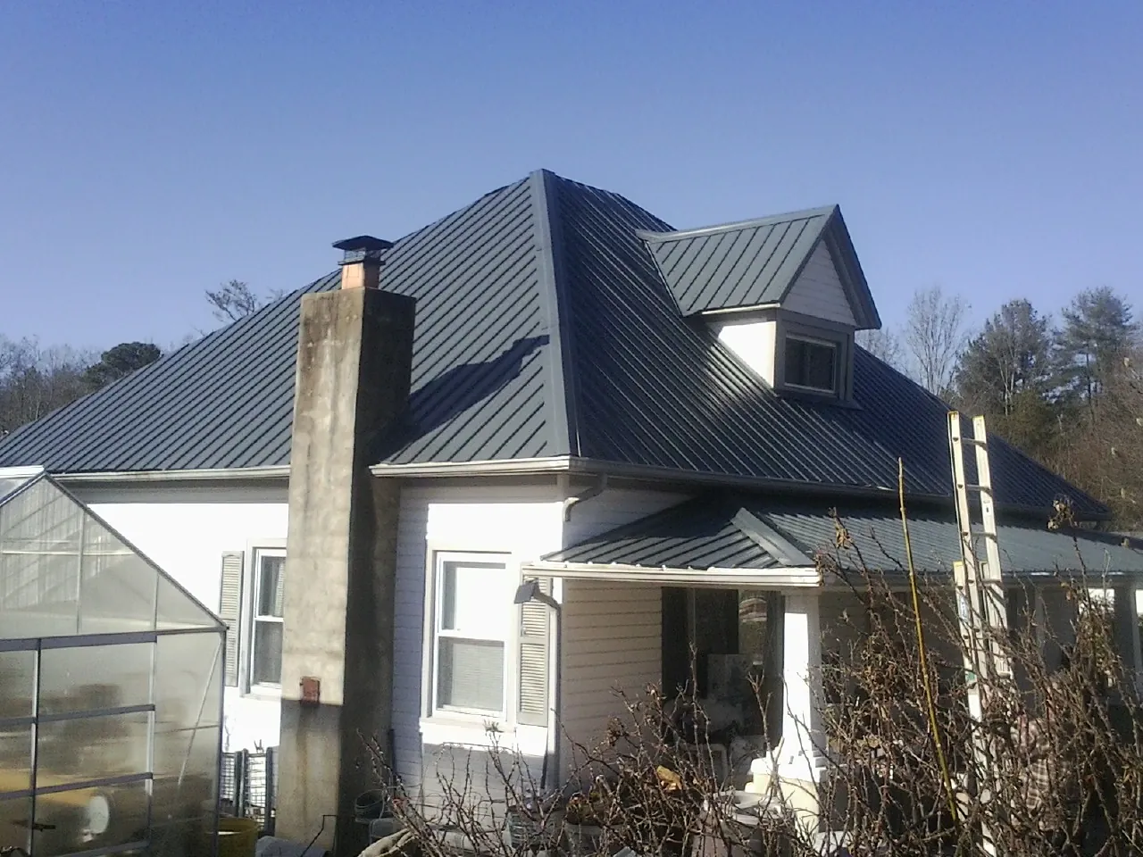 Dark blue standing seam metal roof on a white farmhouse with dormer — Slate & Tile Roof Repair by Roofing Brothers in Magee