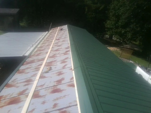 Old rusted panels beside newly installed green metal roofing — Wind Damage Roof Repair by Roofing Brothers in Magee