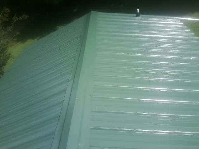 New green metal panels meeting at the ridge of a roof — Flat Roof Repair work by our crew in Magee